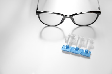 Photo of Single dose eye drops and glasses on white table, space for text