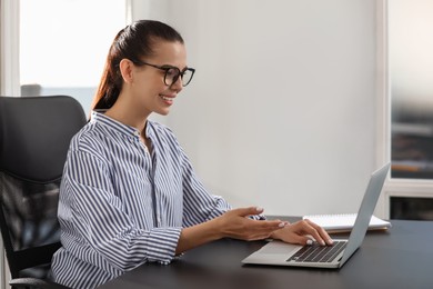 Happy woman using modern laptop at black desk in office