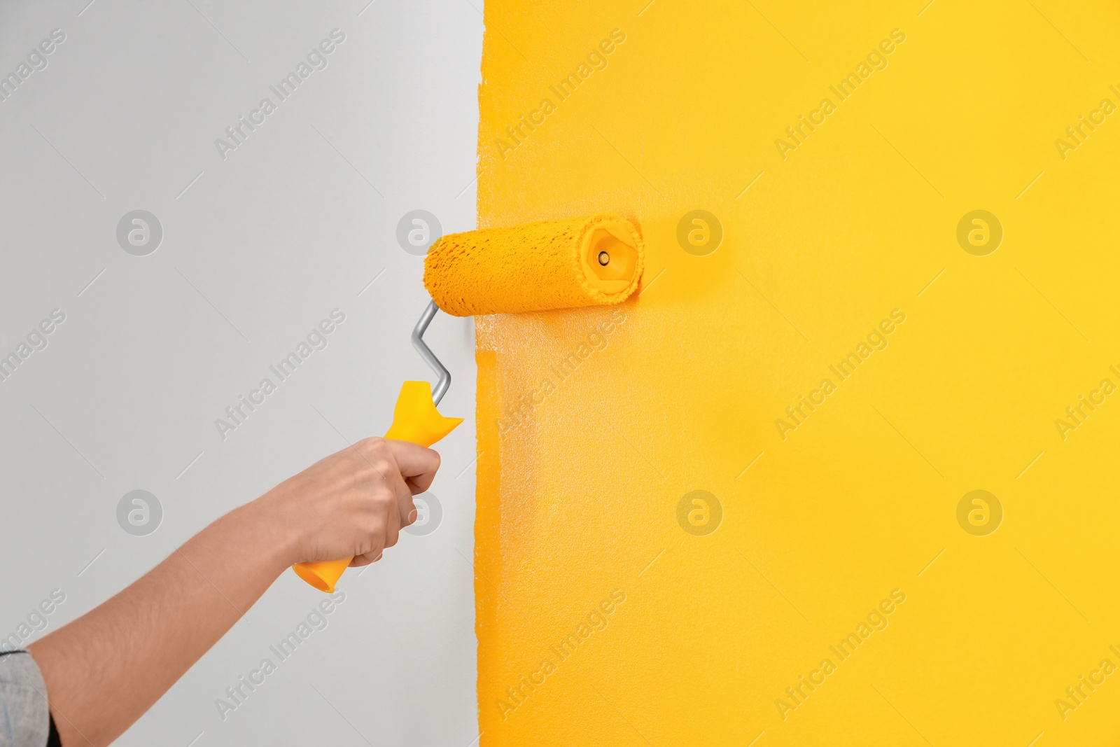 Photo of Woman painting white wall with yellow dye, closeup. Interior renovation