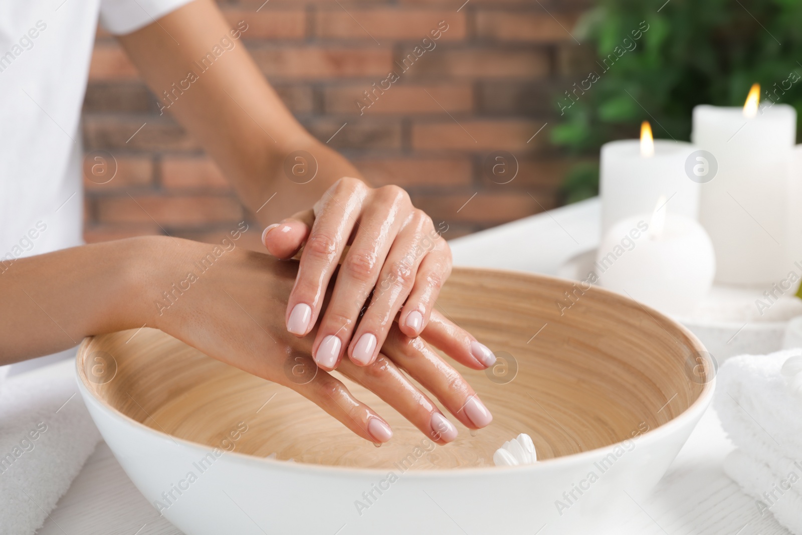 Photo of Woman soaking her hands in bowl of water and flowers on table, closeup with space for text. Spa treatment