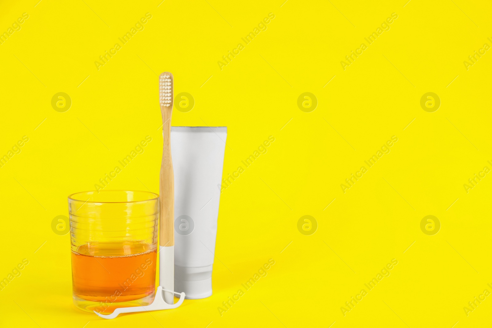 Photo of Mouthwash, toothbrush, paste and dental floss pick on yellow background, space for text