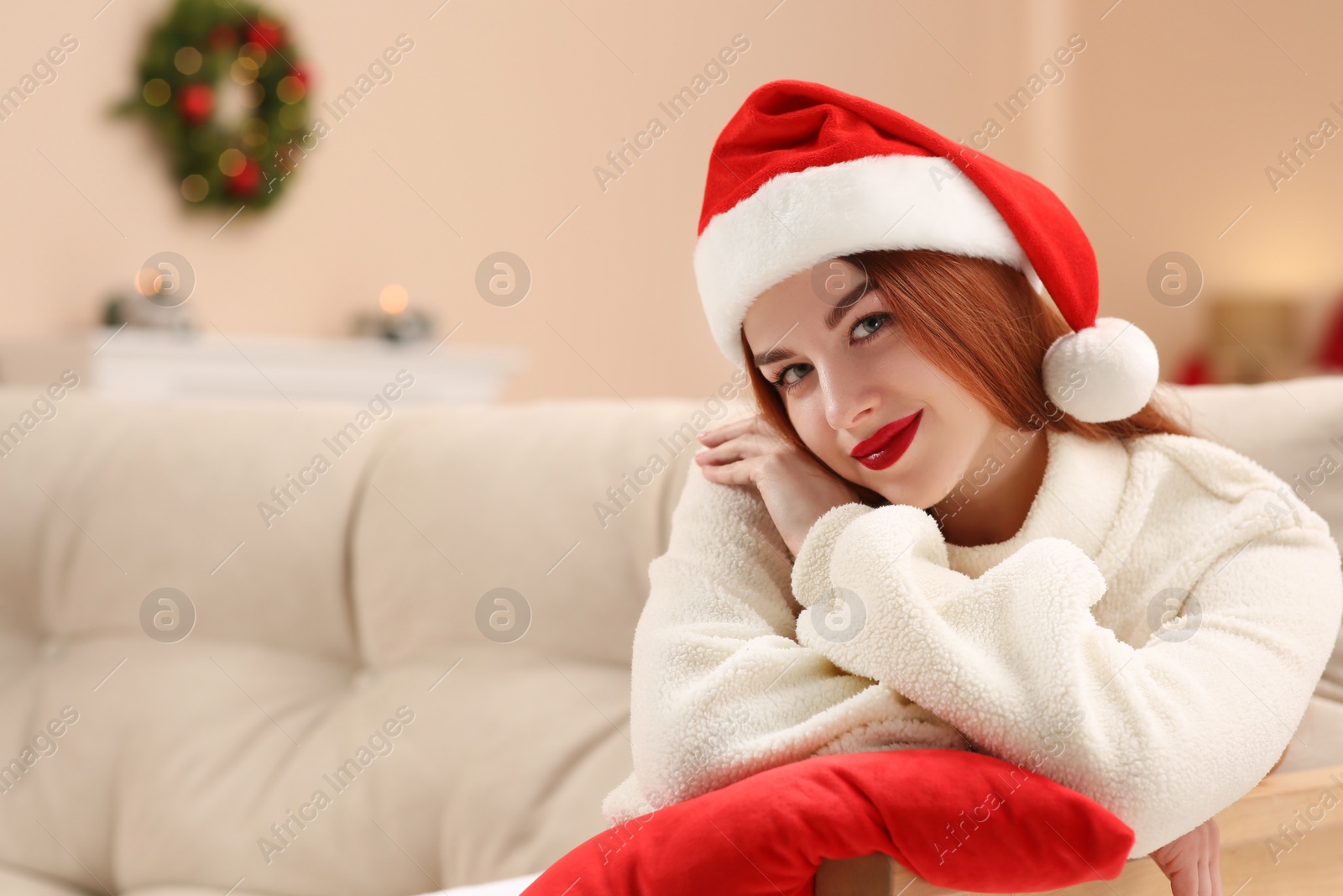 Photo of Beautiful young woman in Santa hat on sofa at home, space for text. Celebrating Christmas