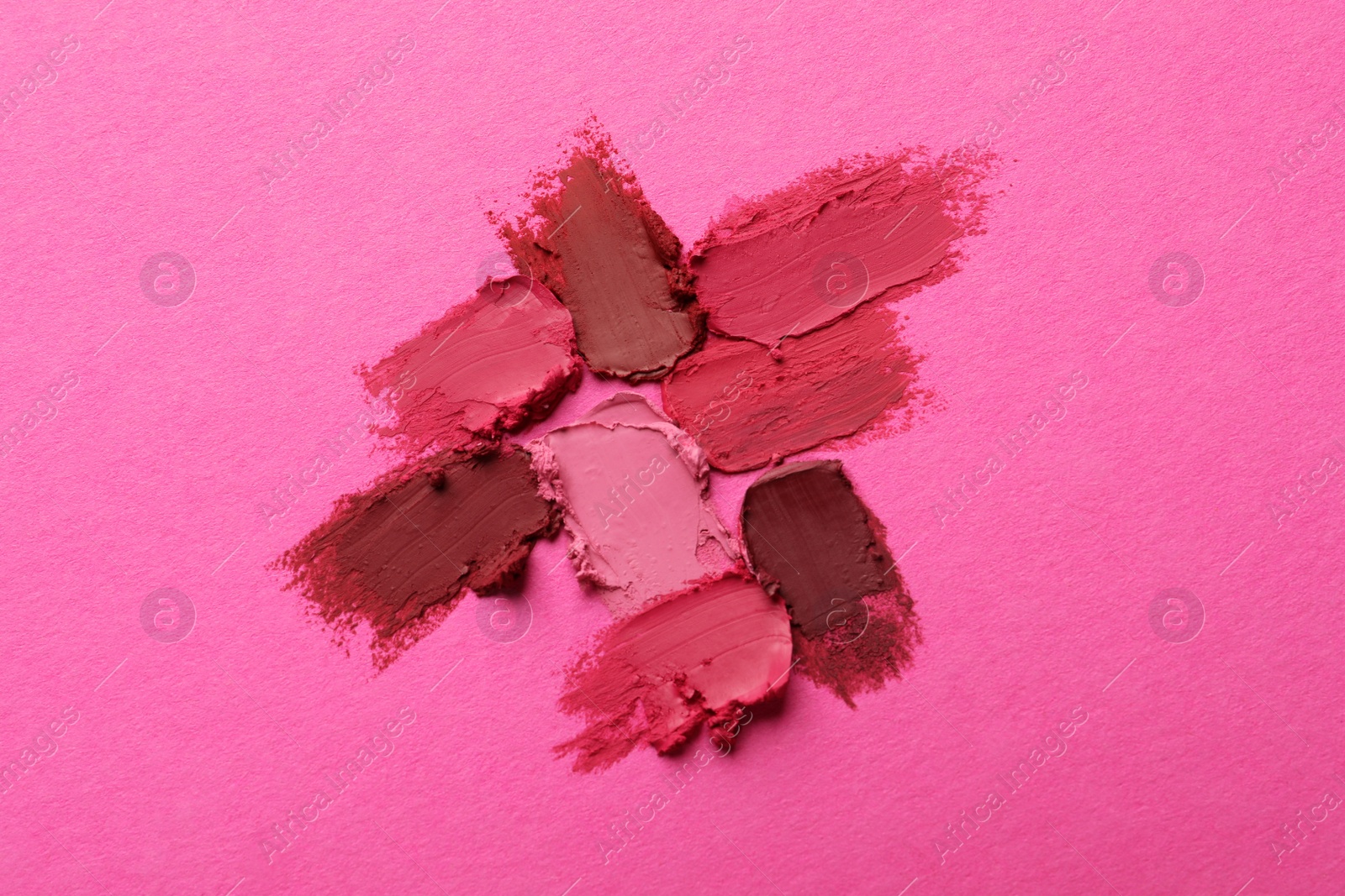 Photo of Smears of beautiful lipsticks on pink background, top view