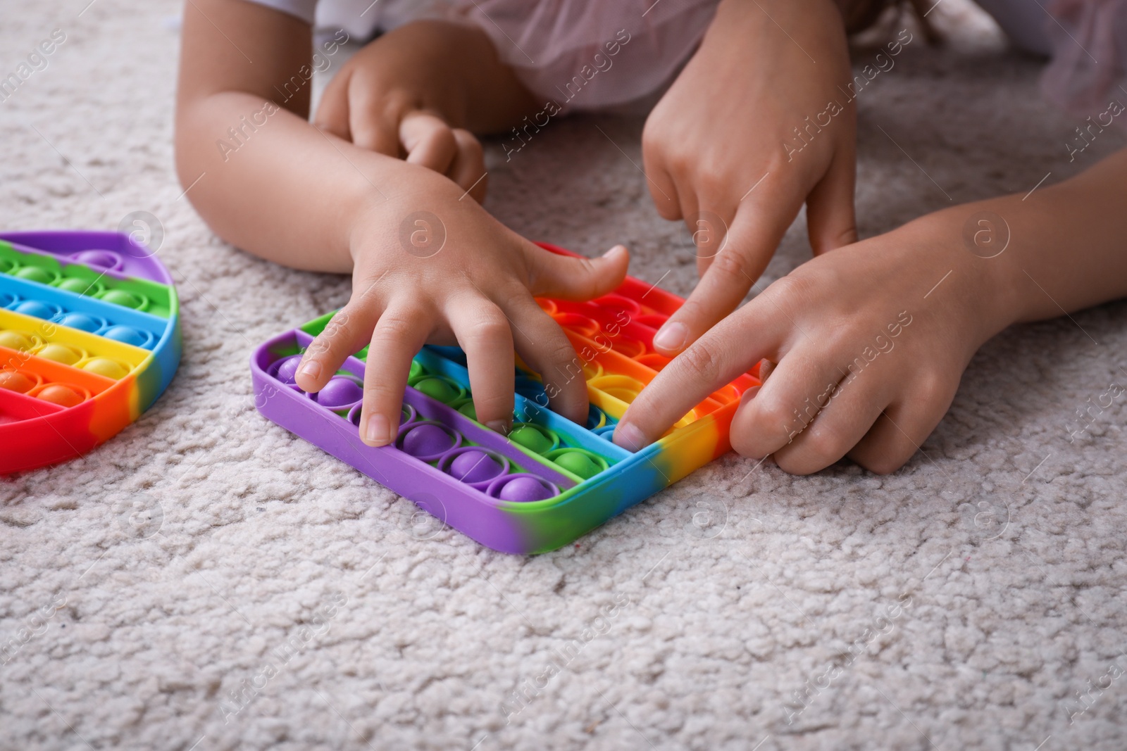 Photo of Little girls playing with pop it fidget toys on floor, closeup