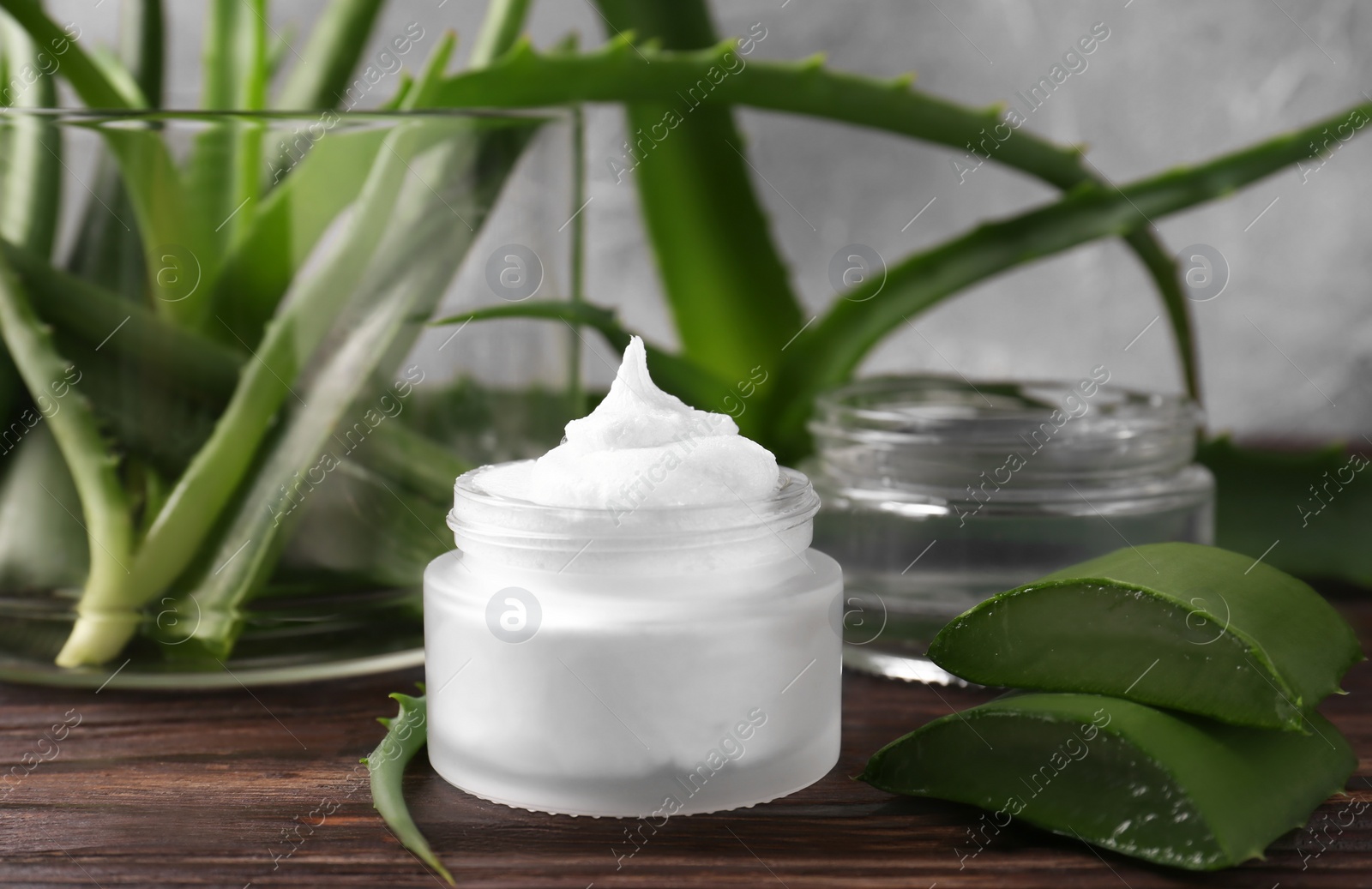 Photo of Jar of cosmetic product and cut aloe vera leaves on wooden table, closeup