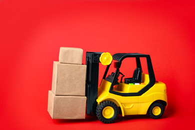 Photo of Toy forklift with boxes on red background Logistics and wholesale concept