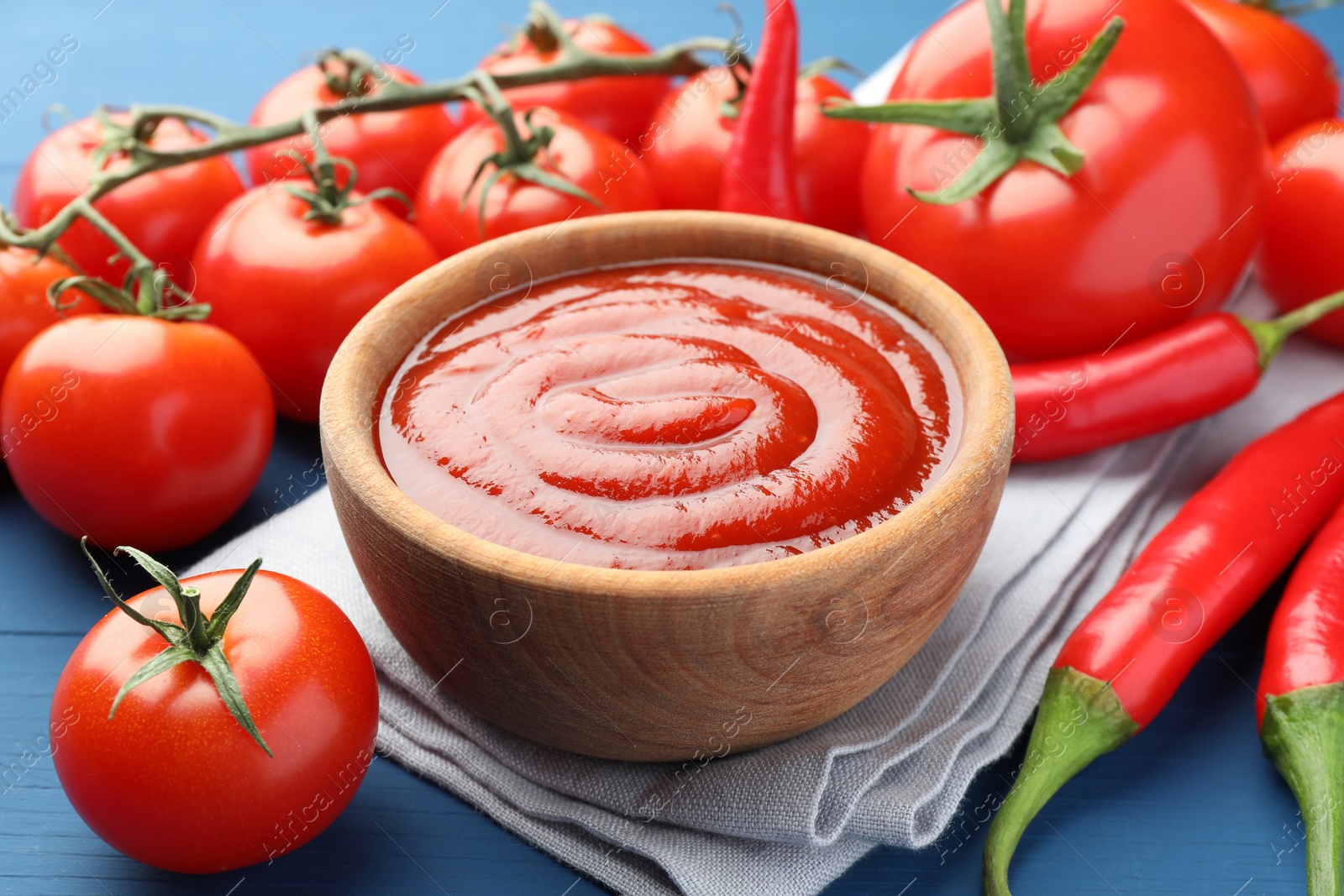 Photo of Bowl of tasty ketchup, tomatoes and peppers on blue wooden table, closeup