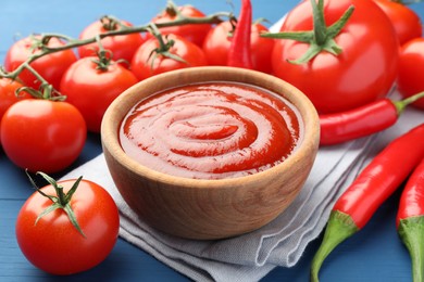 Bowl of tasty ketchup, tomatoes and peppers on blue wooden table, closeup