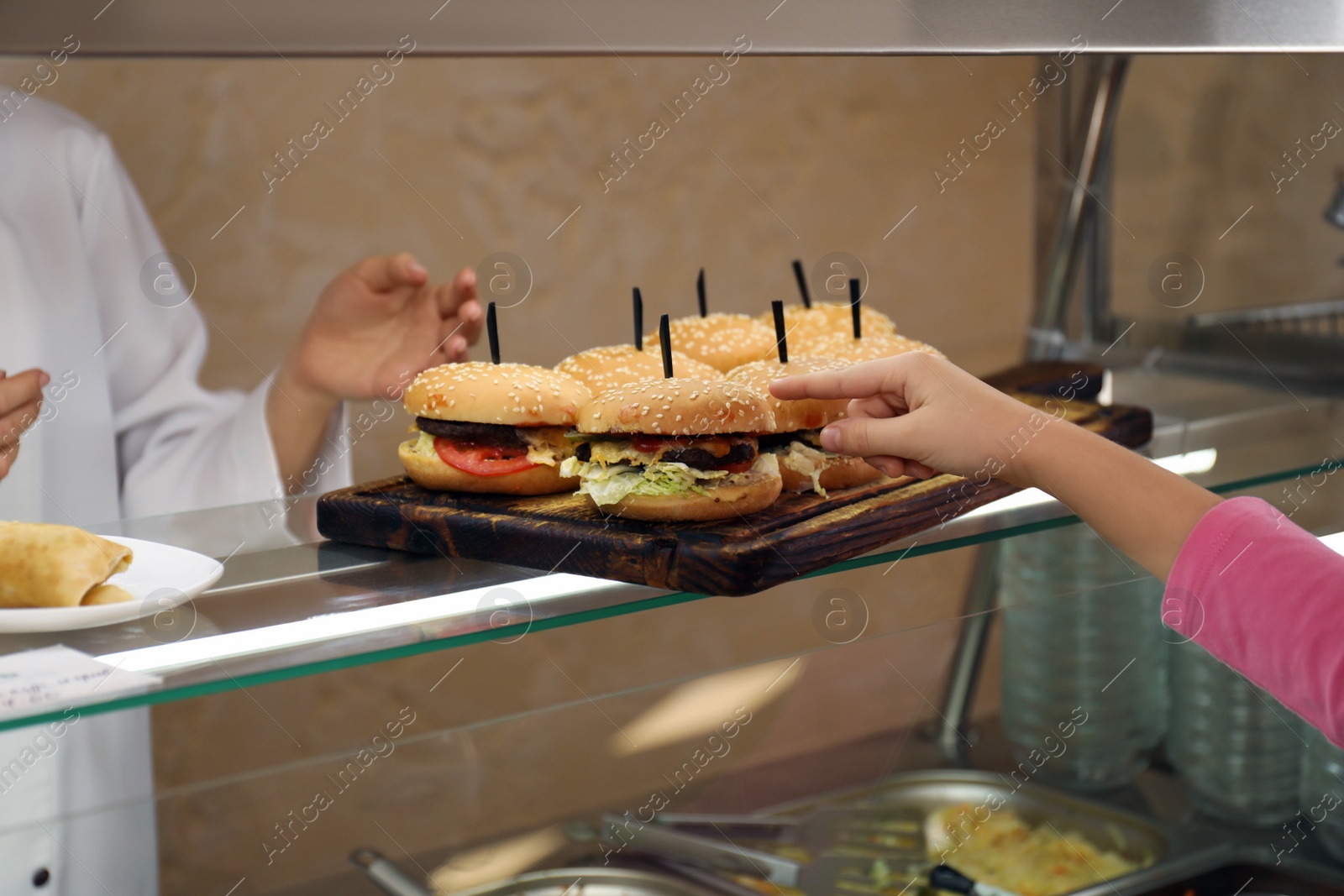 Photo of Little girl taking burger at serving line in canteen. School food