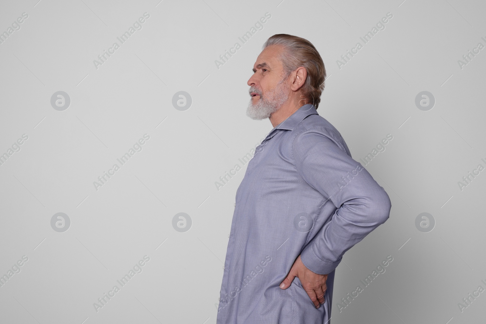 Photo of Senior man suffering from pain in back on light grey background, space for text. Arthritis symptoms