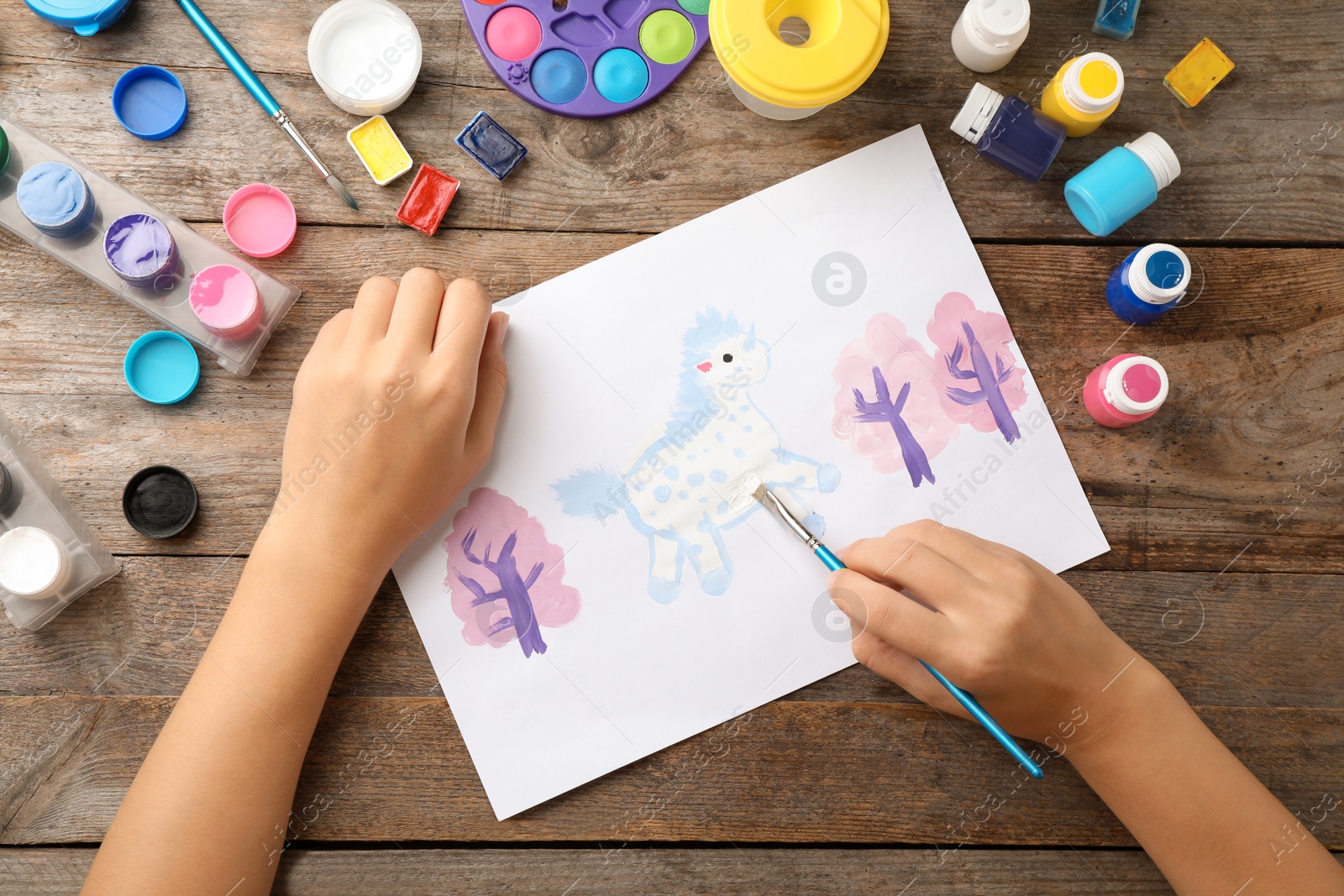 Photo of Girl painting picture of unicorn on table, top view