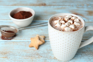 Photo of Delicious hot cocoa drink with marshmallows in cup on light blue wooden table