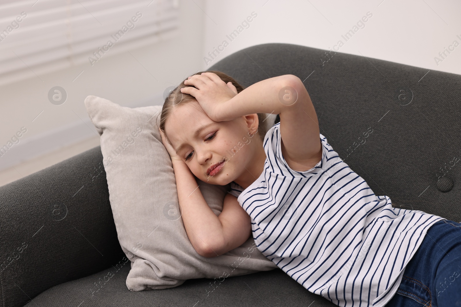 Photo of Little girl suffering from headache on sofa indoors