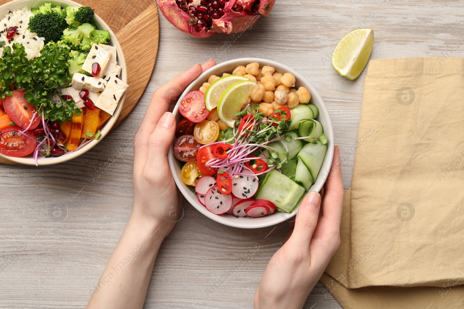 Photo of Woman holding bowl with many different vegetables at white wooden table, top view. Vegan diet