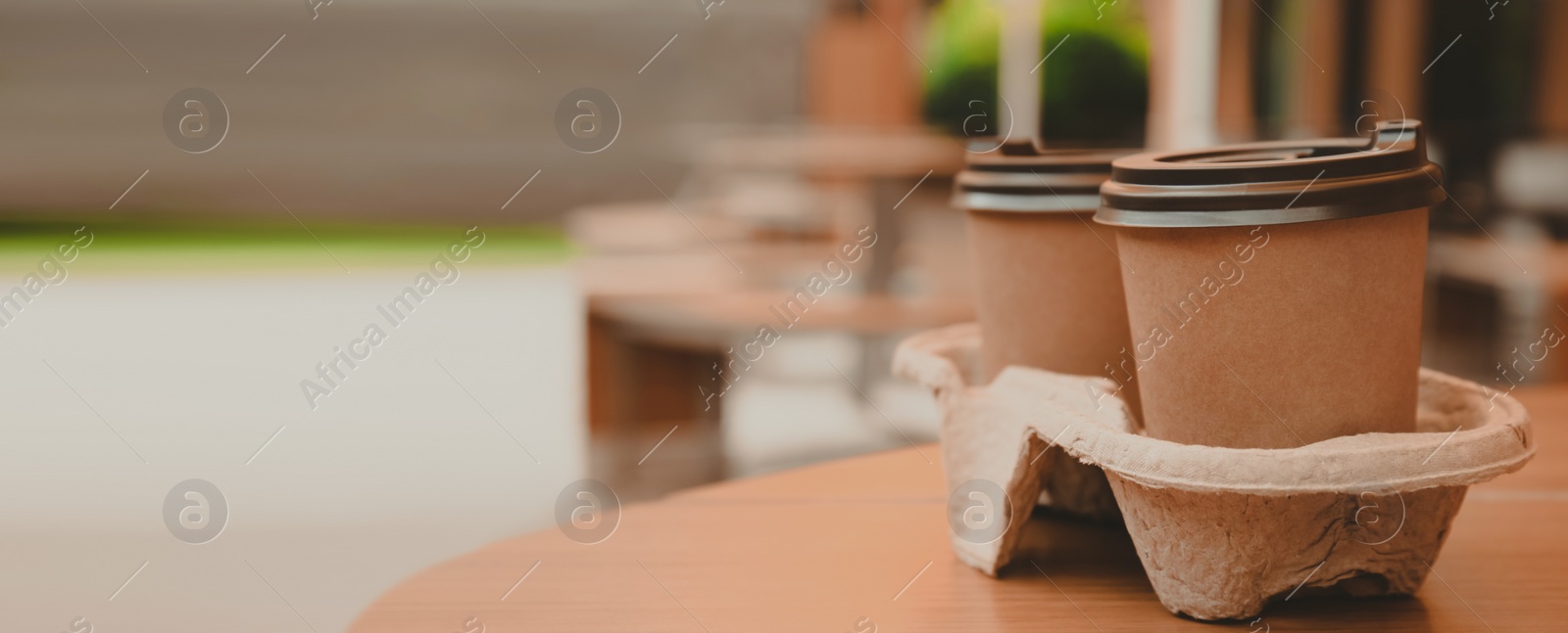 Image of Takeaway paper coffee cups with plastic lids in cardboard holder on wooden table outdoors, space for text. Banner design