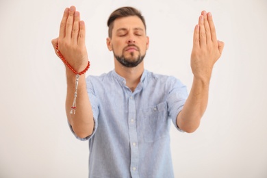 Photo of Muslim man with misbaha praying on light background