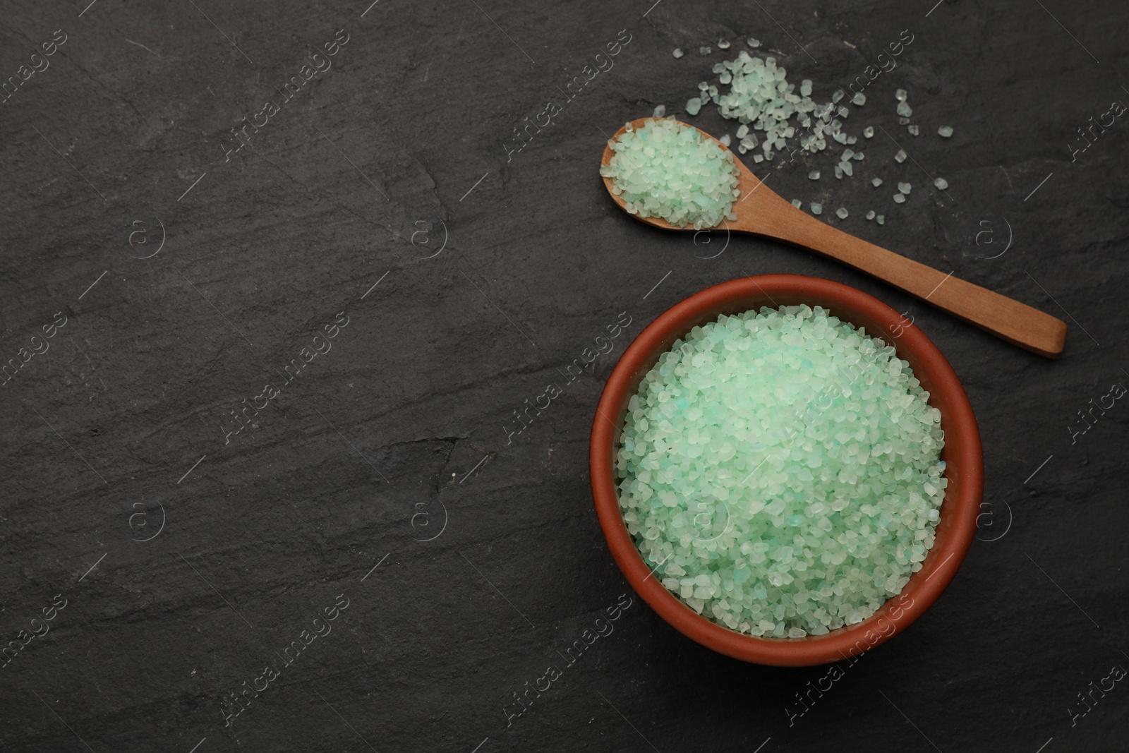 Photo of Bowl and spoon with turquoise sea salt on black table, flat lay. Space for text