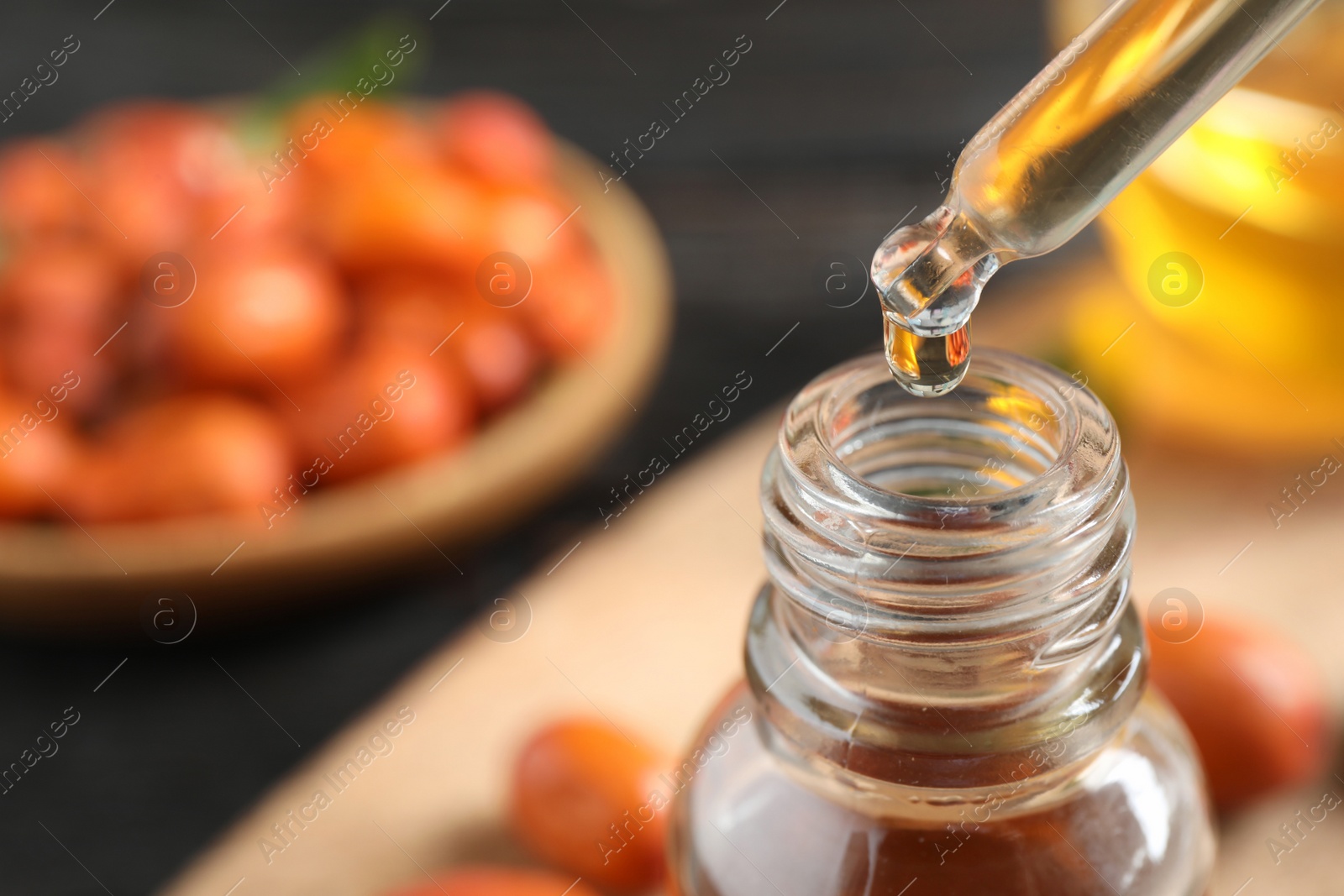 Photo of Dripping jojoba oil from pipette into bottle on blurred background, closeup. Space for text