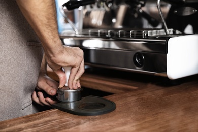 Photo of Barista tamping milled coffee in portafilter at bar counter, closeup. Space for text