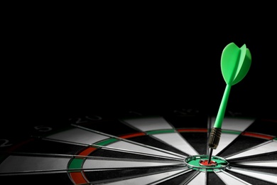 Green arrow hitting target on dart board against black background. Space for text