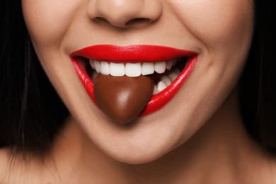 Photo of Young woman with red lips eating heart shaped chocolate candy, closeup