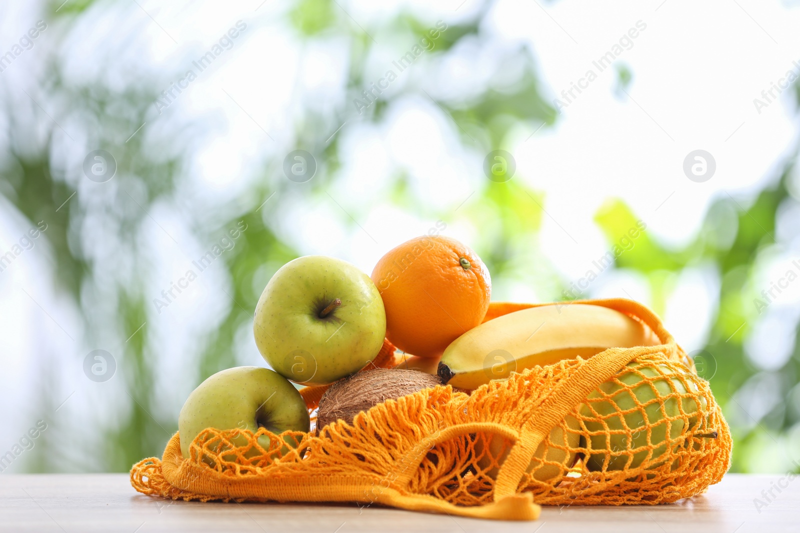 Photo of Net bag with fruits on table against blurred background