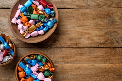 Photo of Candies in colorful wrappers on wooden table, flat lay. Space for text