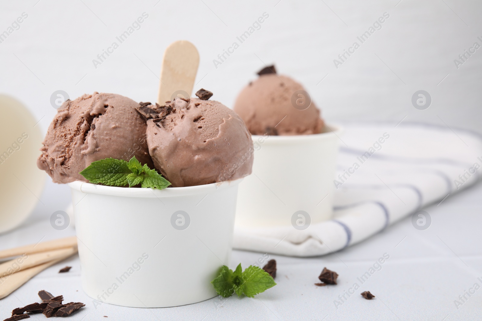 Photo of Paper cups with tasty chocolate ice cream on white tiled table, closeup. Space for text