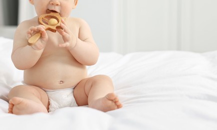 Cute baby boy with wooden rattle on bed at home. Space for text