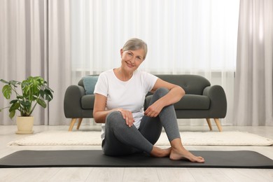 Happy senior woman sitting on mat at home. Yoga practice