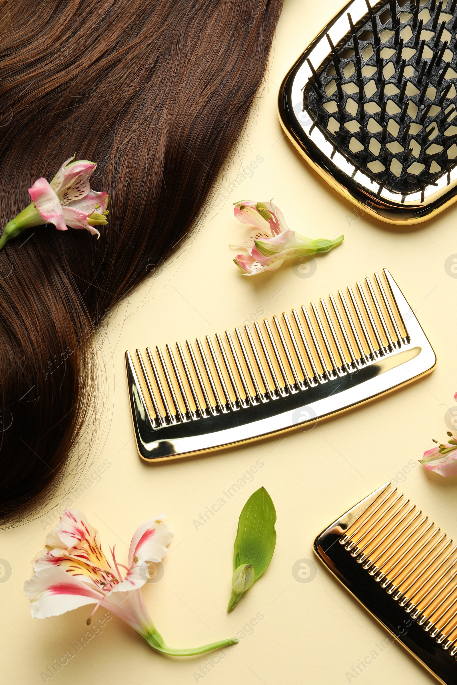 Photo of Hairdresser tools. Brown hair lock, combs, brush and flowers on pale yellow background, flat lay