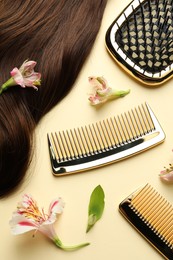 Hairdresser tools. Brown hair lock, combs, brush and flowers on pale yellow background, flat lay