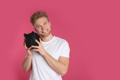 Young man with piggy bank on color background, space for text. Money saving