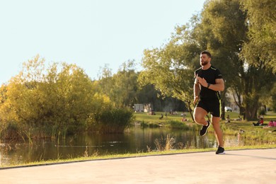 Photo of Young man running near pond in park. Space for text