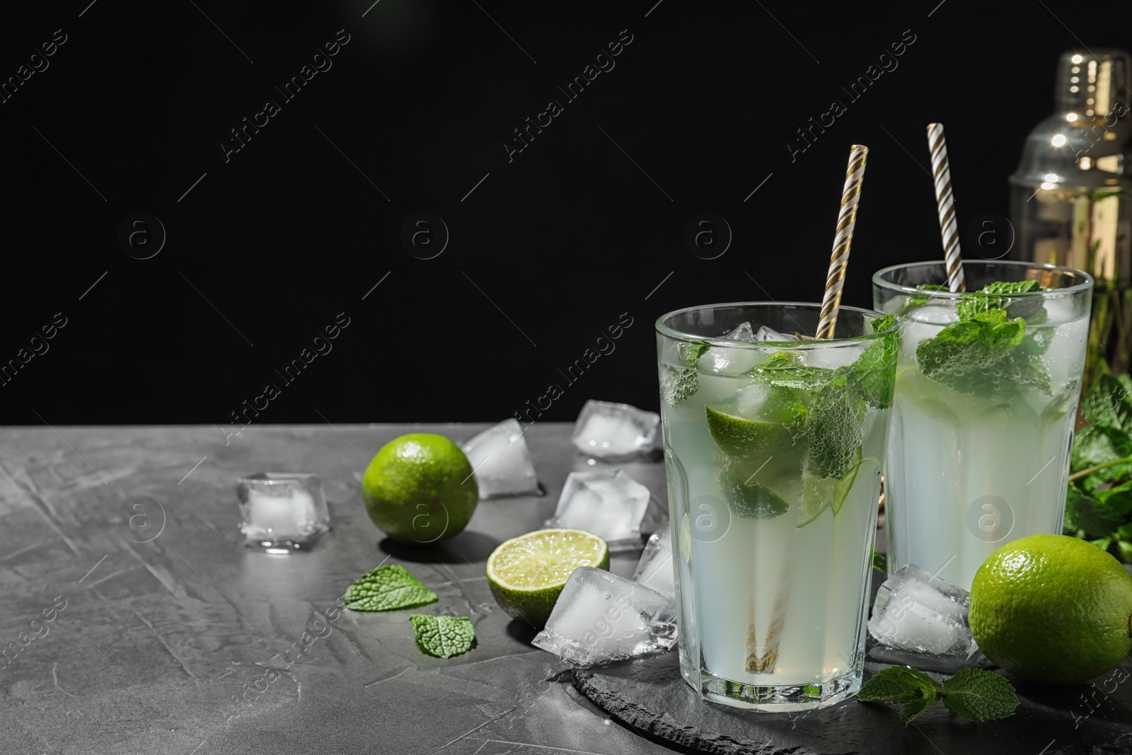 Photo of Glasses of delicious Mojito cocktail with ice and mint on grey table against black background. Space for text