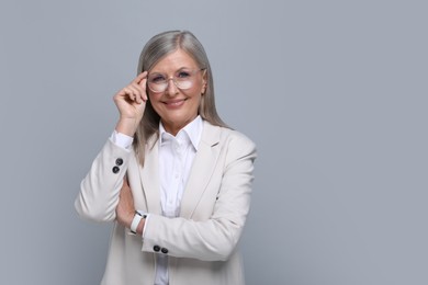 Portrait of beautiful senior woman in glasses on grey background. Space for text