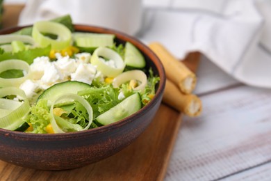 Photo of Bowl of tasty salad with leek and cheese on white wooden table, closeup. Space for text