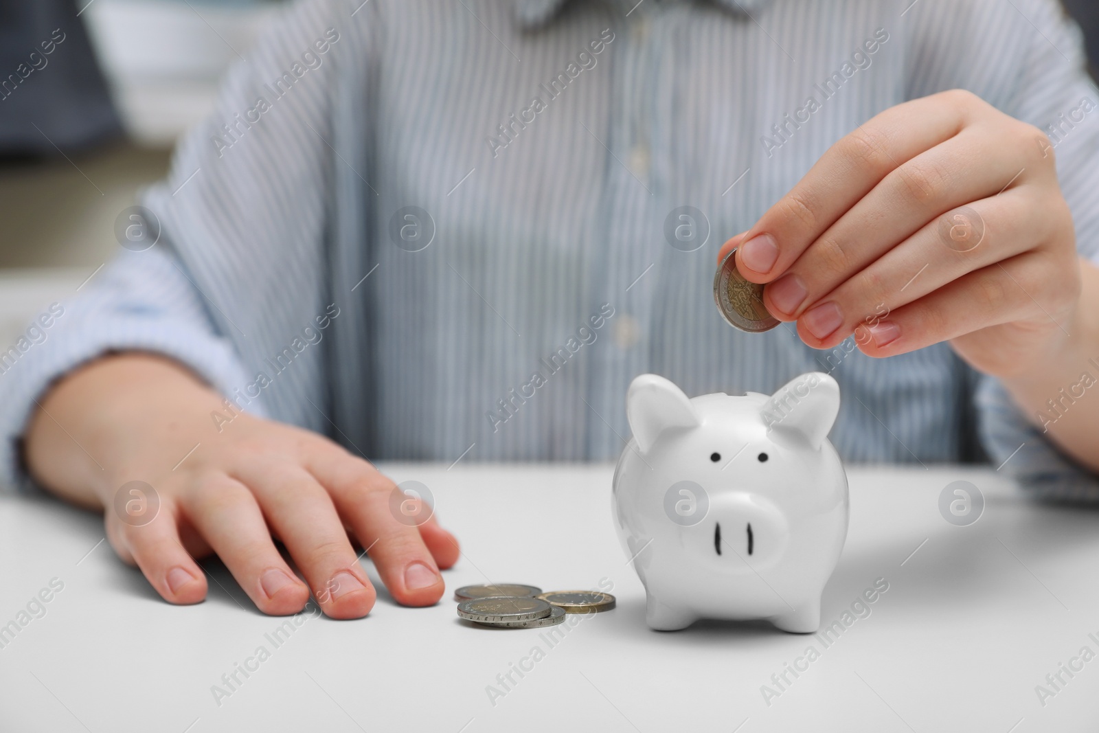 Photo of Woman putting coin into ceramic piggy bank at white wooden table, closeup. Financial savings