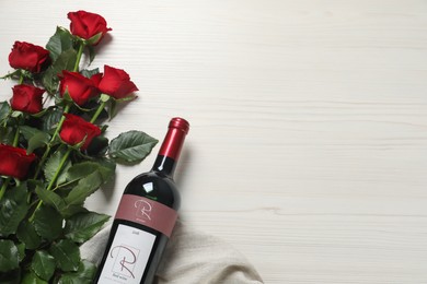 Bottle of red wine and beautiful roses on white wooden table, flat lay. Space for text