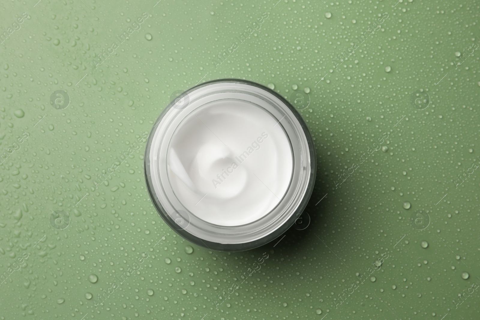 Photo of Glass jar of face cream on wet green surface, top view