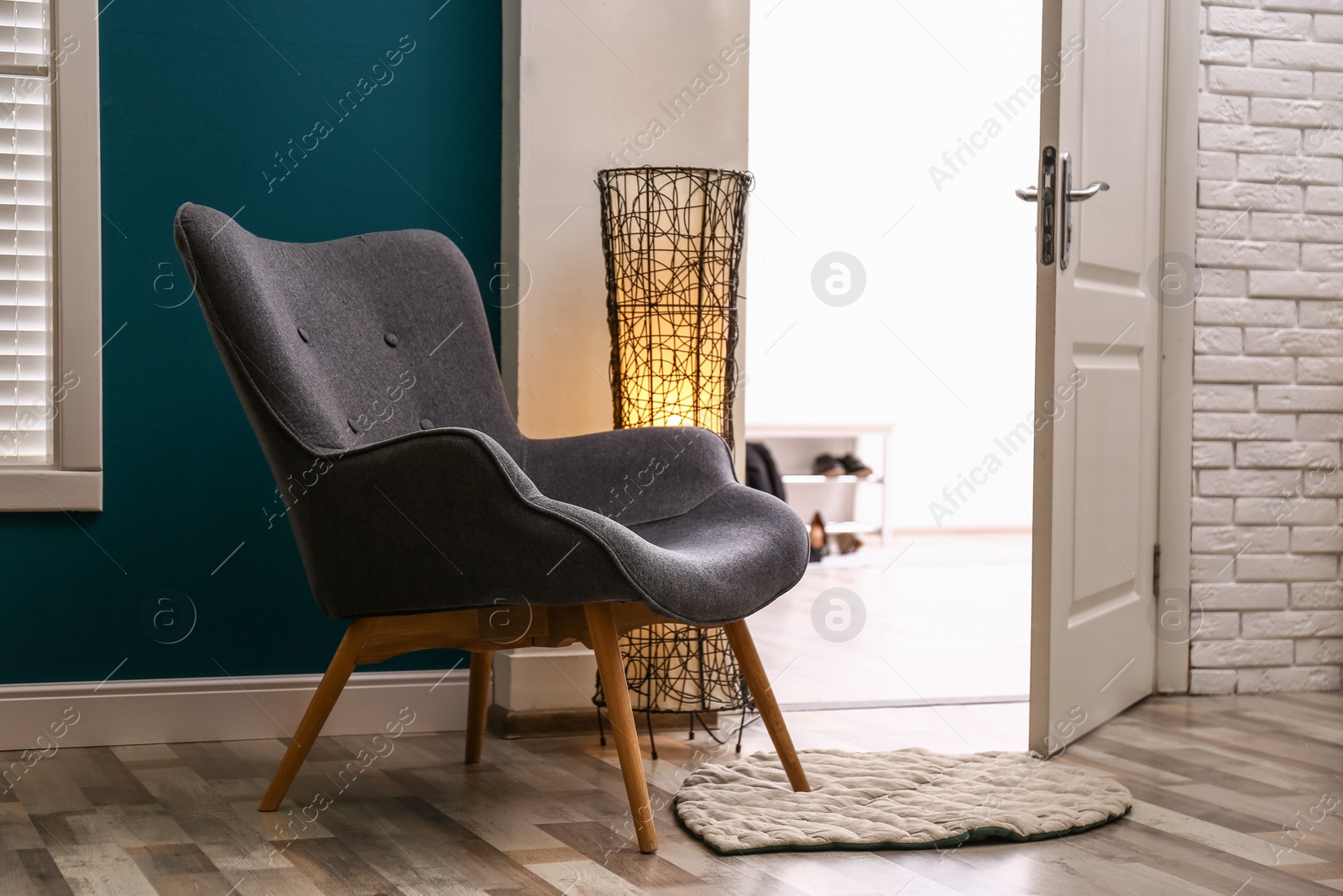 Photo of Comfortable armchair with floor lamp and rug indoors