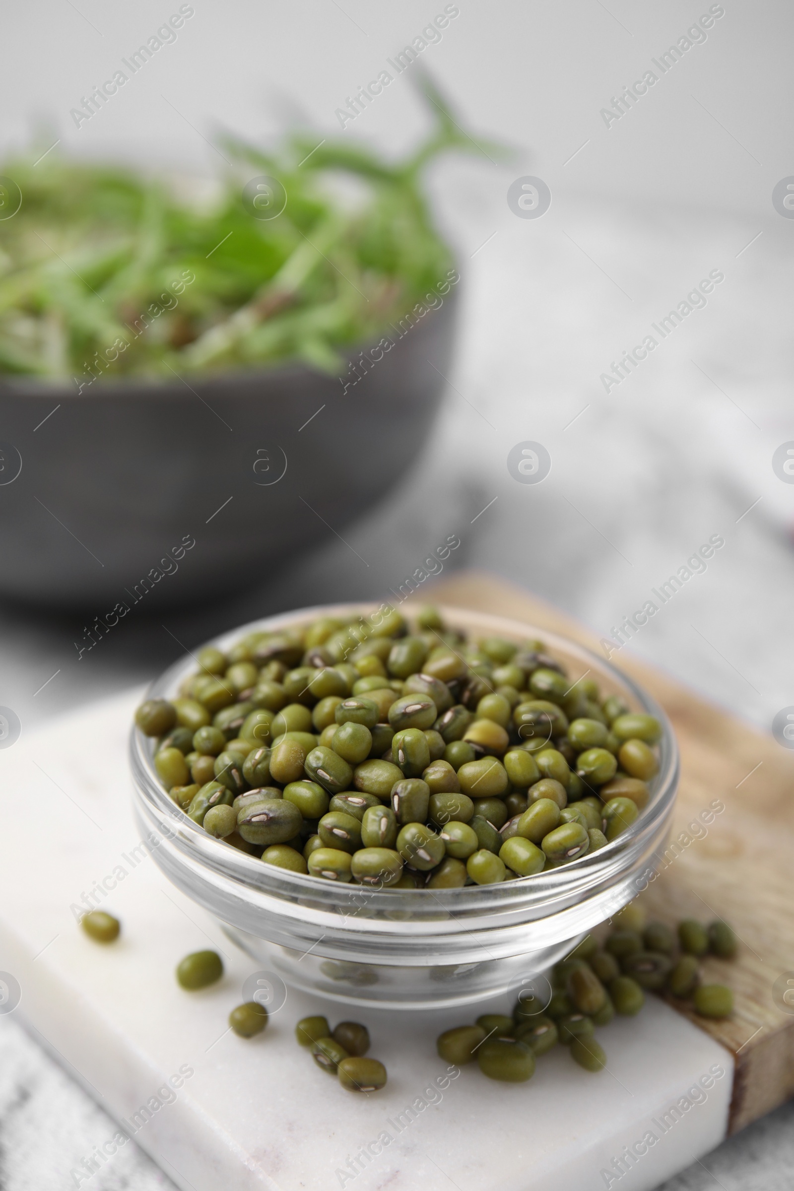 Photo of Glass bowl with mung beans and coaster on white textured table, closeup