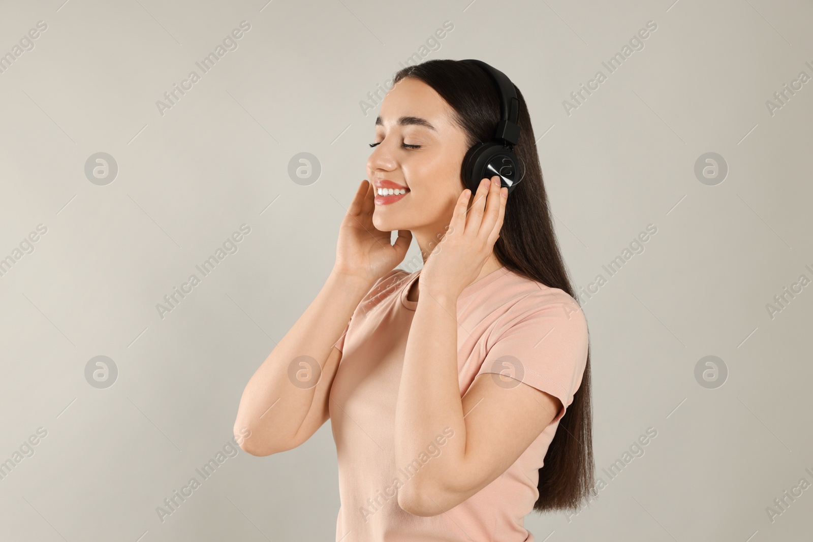 Photo of Happy woman in headphones enjoying music on grey background