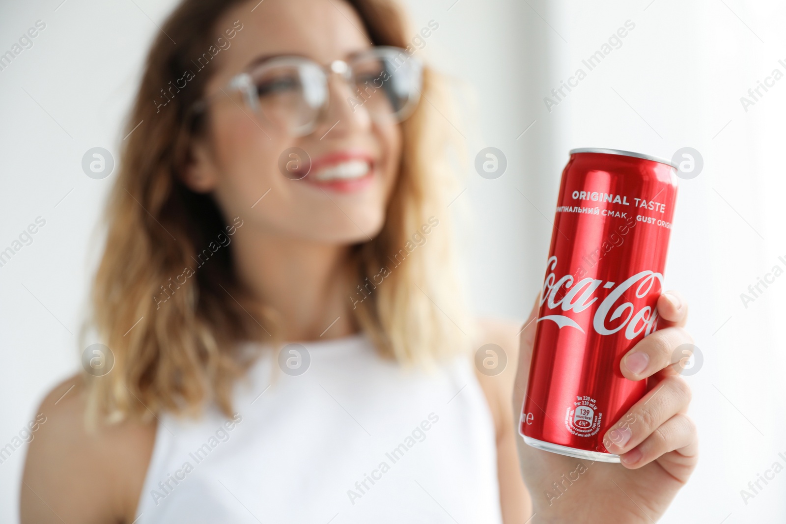 Photo of MYKOLAIV, UKRAINE - NOVEMBER 28, 2018: Young woman with Coca-Cola can indoors, closeup