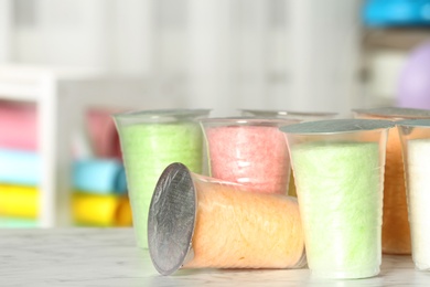 Plastic cups with cotton candy on table against blurred background