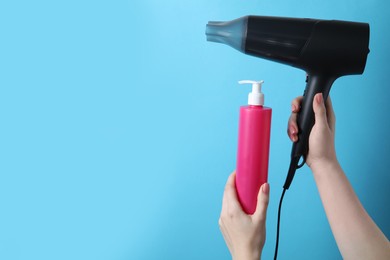 Woman holding spray bottle with thermal protection and hairdryer on light blue background, closeup. Space for text