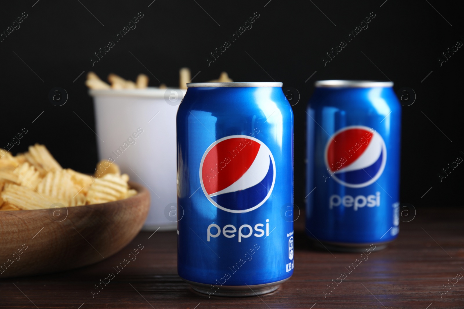 Photo of MYKOLAIV, UKRAINE - FEBRUARY 15, 2021: Cans of Pepsi and snack on wooden table