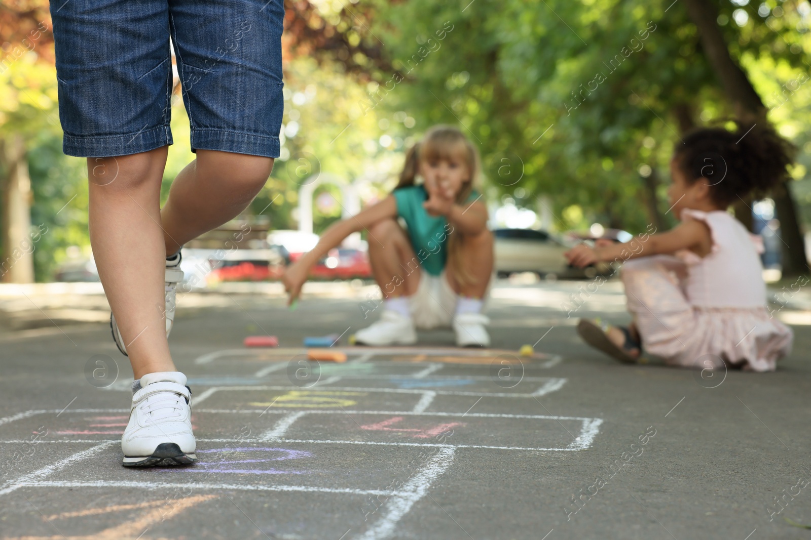 Photo of Little children playing hopscotch drawn with chalk on asphalt outdoors, closeup