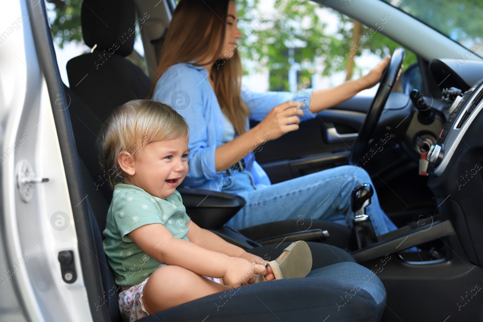 Photo of Mother with cigarette and child in car, focus on little girl. Don't smoke near kids