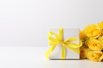 Beautiful bouquet of yellow roses and gift box on white background, space for text